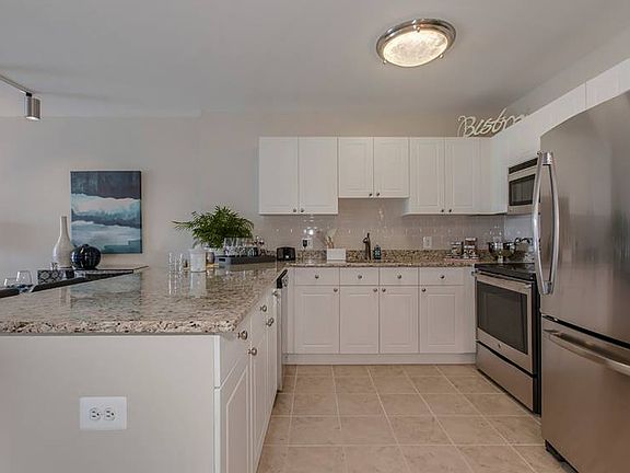 Open concept kitchen with white cabinetry, cream tile backsplash, stainless-steel appliances, granite countertops and hard surface flooring