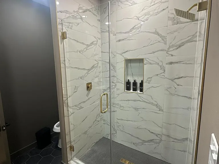 Walk-in shower with large-format tile surround, frameless glass enclosure, built-in niche, and rainfall showerhead.
