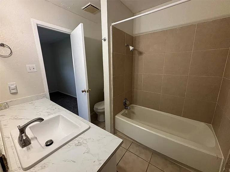 Bathroom featuring a white vanity with a patterned countertop, an integrated rectangular sink with a brushed nickel faucet, a white bathtub, and tan tile shower surround