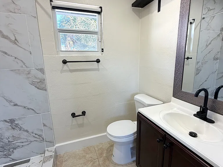 Features a newly installed toilet and a bright, impeccably clean bathroom. (Angle 2)