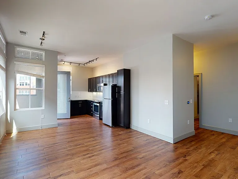 Apartment kitchen with stainless steel appliances, dining and living room with wood-style flooring.