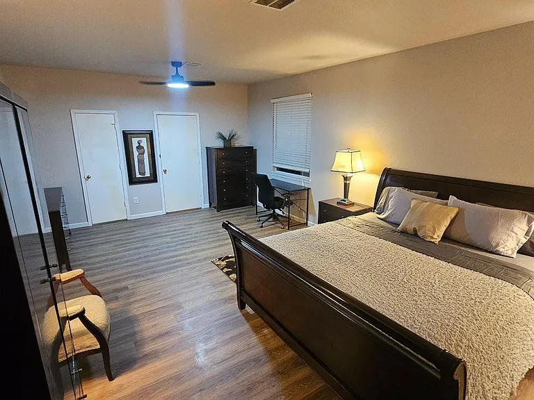 Spacious furnished bedroom with a full bed, dresser, wardrobe storage, and a dedicated desk area near the window.