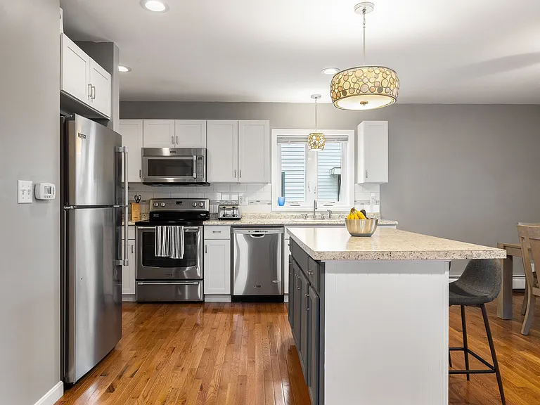 Kitchen Island, Breakfast Bar, Granite Countertops, Stainless Steel Appliances, White Shaker Cabinets, Recessed Lighting, Pendant Lighting, Hardwood Flooring, Tile Backsplash.