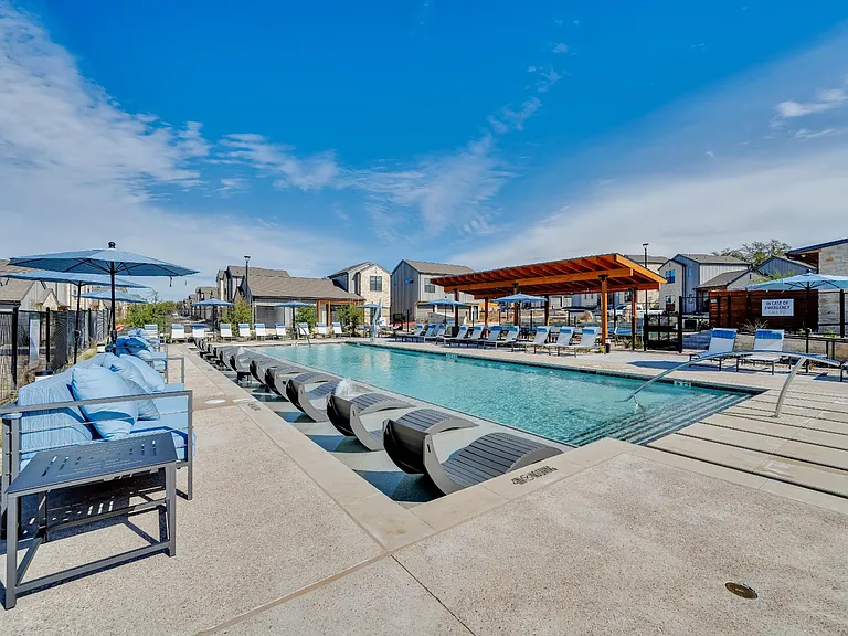 A sunny day at the pool with blue lounge chairs and a clear sky.