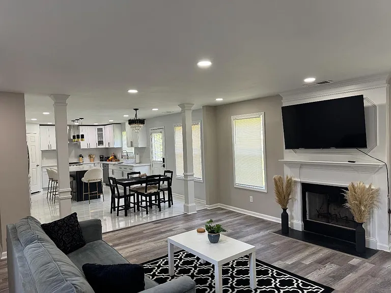 Open-concept living area with fireplace, wall-mounted TV, and adjoining dining space that flows into a well-equipped kitchen.