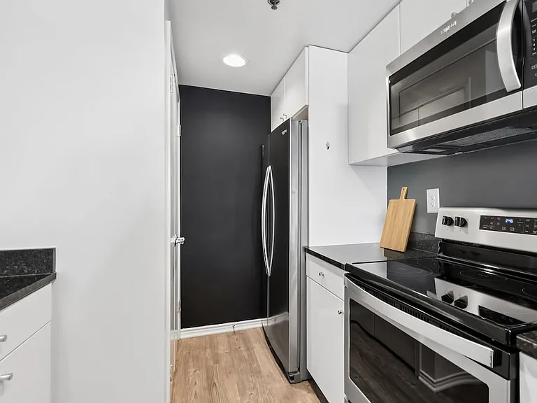 Renovated Package I kitchen with white cabinetry, black granite countertops, stainless steel appliances, and hard surface flooring