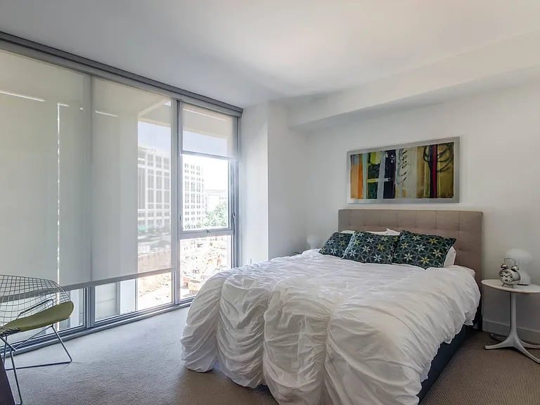Wake up to city views in this bright bedroom featuring floor-to-ceiling windows, a stylish bed, and bold modern art.