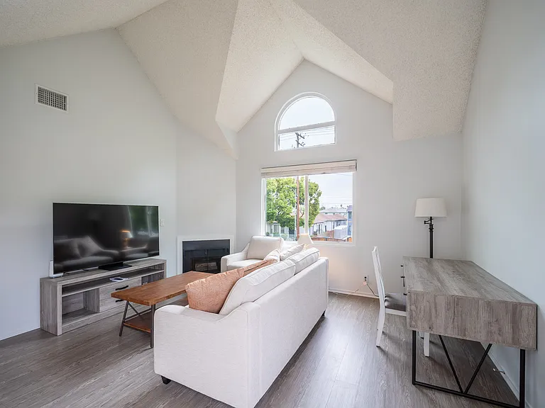 Furnished living room with gas FP, vaulted ceilings, desk with chair, sofa, chair, coffee tables, TV and TV console.