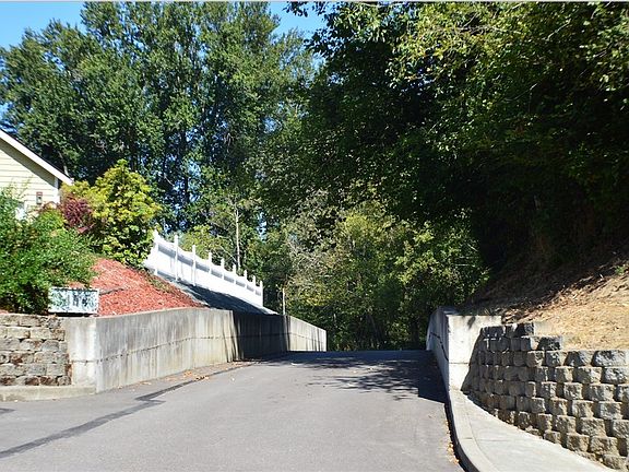 Entrance, long paved drive to property in back. Concrete walls line the driveway. 