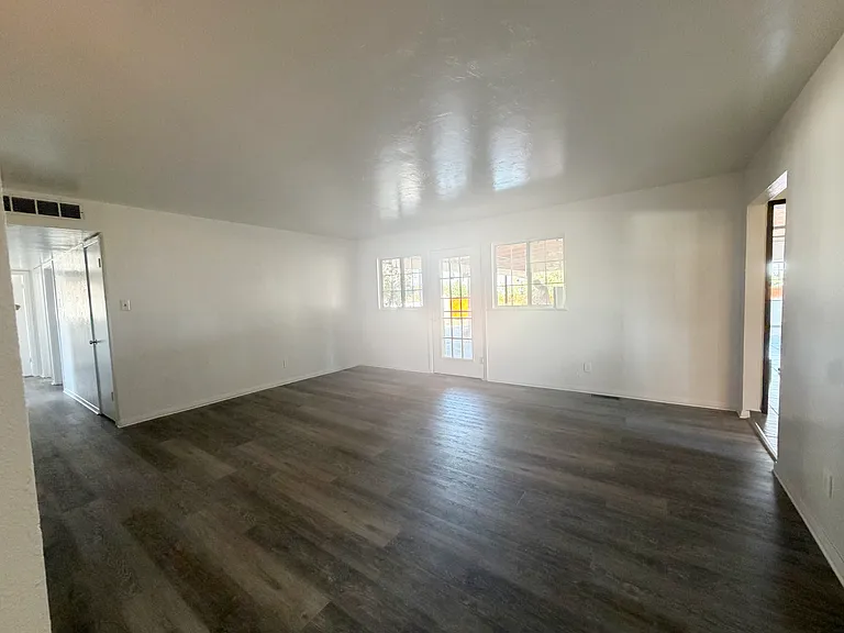The large living room features new slate vinyl flooring that is spacious enough for 3 large sofas, with entry to the backyard. Point of view from the kitchen entry.