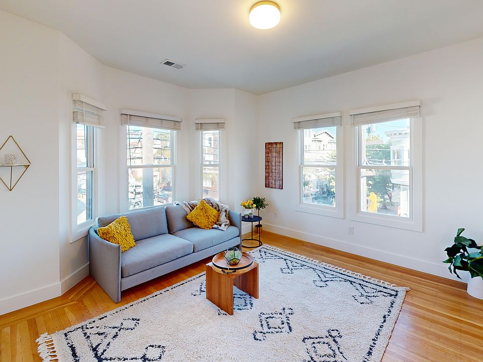 Serene and inviting living room with a large window, allowing natural light to flood the space, dominated by a sofa, adorned with two throw pillows, a wooden coffee table