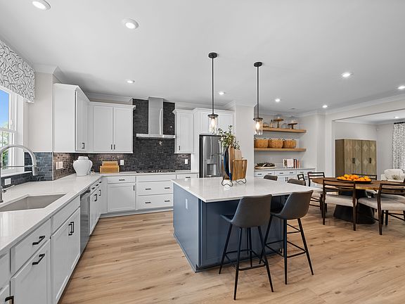 A modern, open-concept kitchen with white cabinets, a large island, and a dining area with a wooden