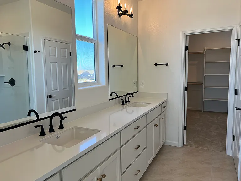 Primary Bath: A spa-inspired ensuite with dual vanities, a frameless glass walk-in shower, and designer black fixtures.