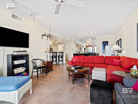 Living room with light tile patterned flooring, crown molding, ceiling fan with notable chandelier, and track lighting