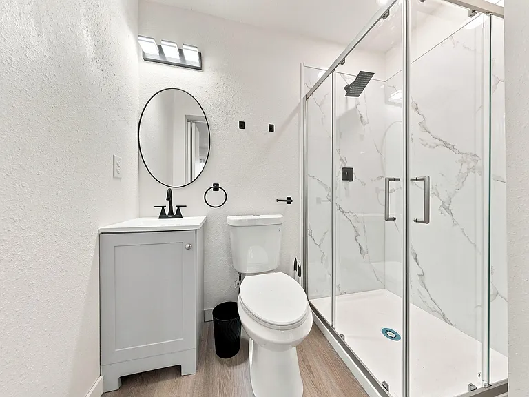 Updated bathroom with a single-sink vanity, round mirror, and glass-enclosed shower with tile-look surround.