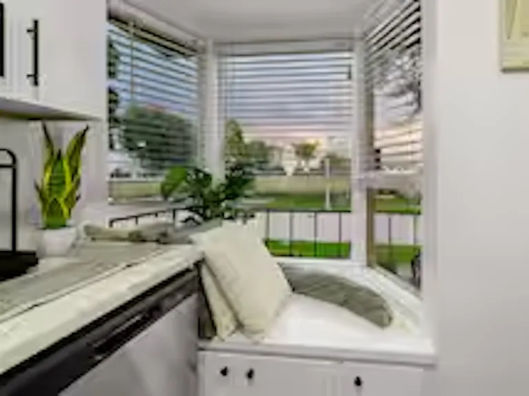 Modern kitchen with white cabinetry, stainless steel appliances, and stone benchtops, featuring a coffee machine, blender, stove cooktop, and plenty of natural light.