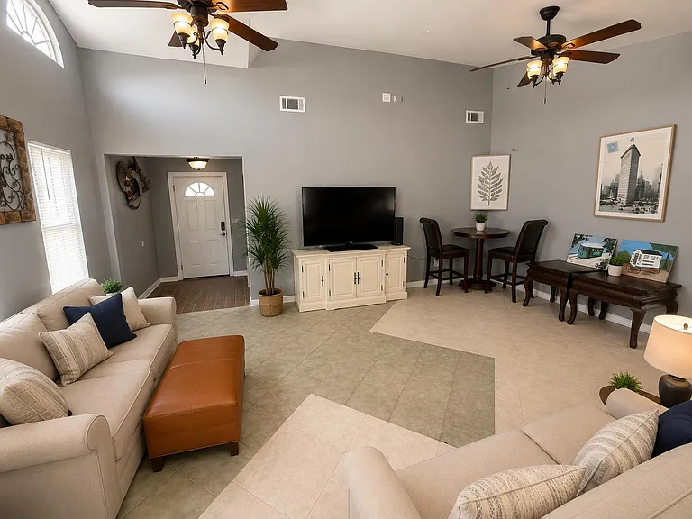 Open living area with vaulted ceiling, ceiling fans, lounge seating, and a TV console, plus a small dining nook.