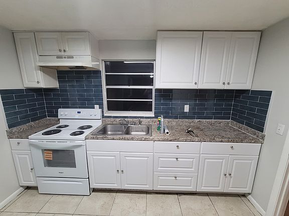 Modern kitchen with sleek white cabinets, blue tile backsplash, white stove, and a double divided sink. Bright, stylish, and designed for both function and visual appeal.