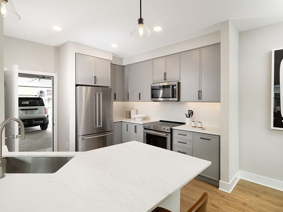Signature Collection kitchen with stainless steel appliances, white quartz countertop, grey cabinetry, white quartz backsplash, hard surface flooring, and attached garage