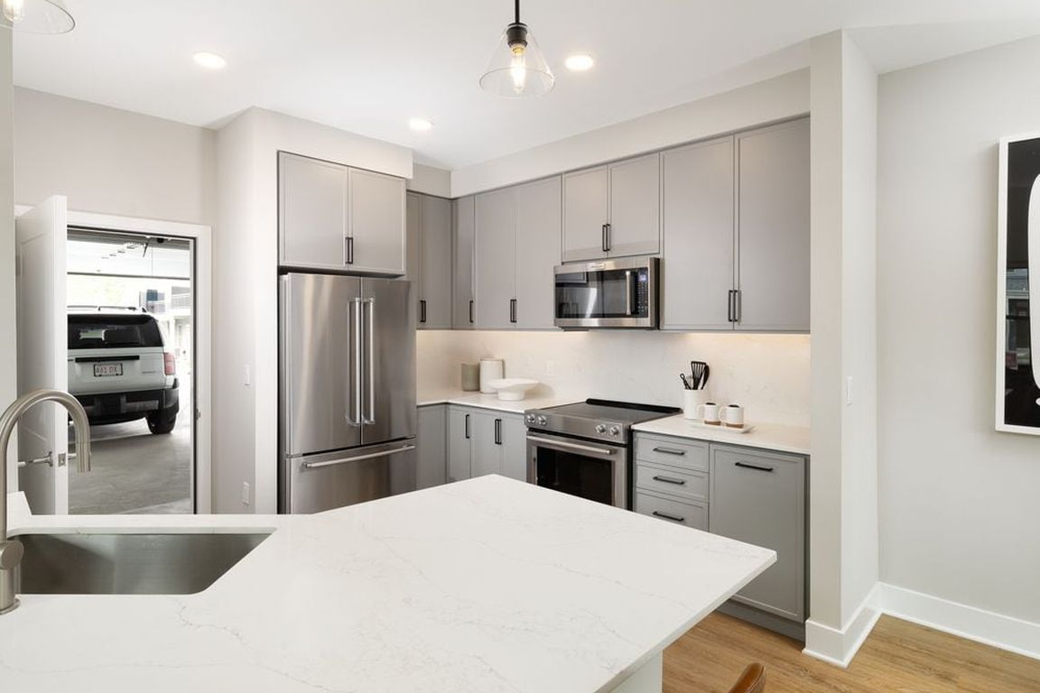 Signature Collection kitchen with stainless steel appliances, white quartz countertop, grey cabinetry, white quartz backsplash, hard surface flooring, and attached garage