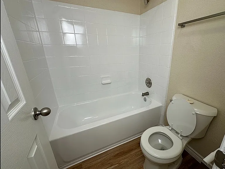 Modern bathroom featuring a sleek bathtub, pristine white tiles, and elegant wood flooring. Modern bathroom featuring a sleek bathtub, pristine white tiles, and elegant wood flooring.