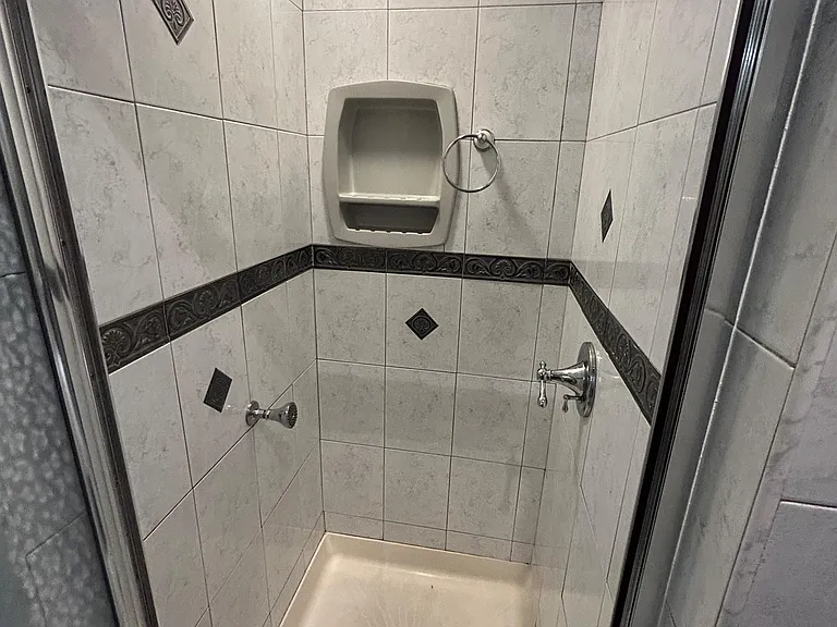 Tiled walk-in shower with glass enclosure, built-in soap niche, and multiple shower fixtures for added convenience.