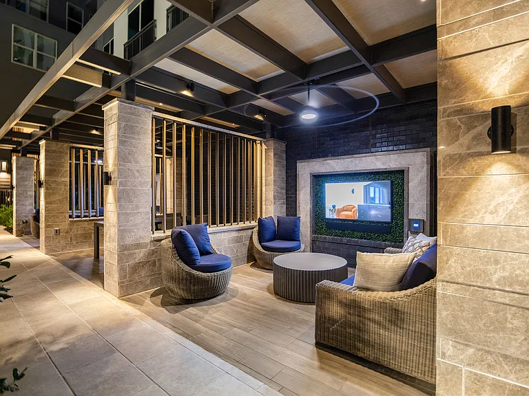 Luxurious outdoor lounge with modern wicker seating, ambient lighting, and a built-in entertainment screen.