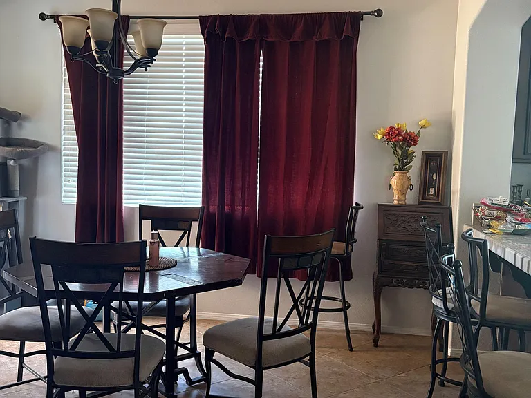 Dining area with a table for four, pendant lighting, and a large window with blinds and drapery for natural light.