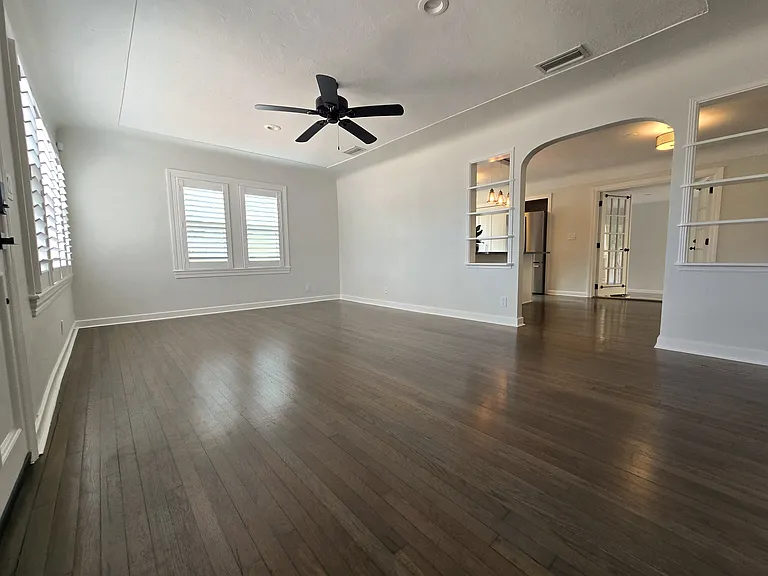 Living room (no furniture), showing arched doorway, built-in shelving, hardwood floors, white plantain shutters and ceiling fan