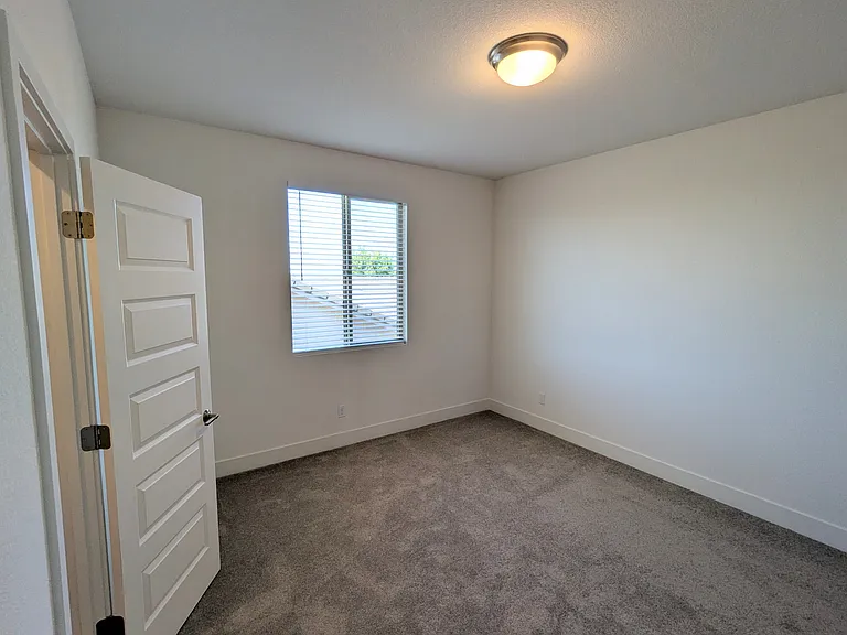 This comfortable secondary bedroom offers a bright, inviting atmosphere. It features a spacious walk-in closet and large windows with custom horizontal blinds, providing the perfect balance of privacy and natural light.