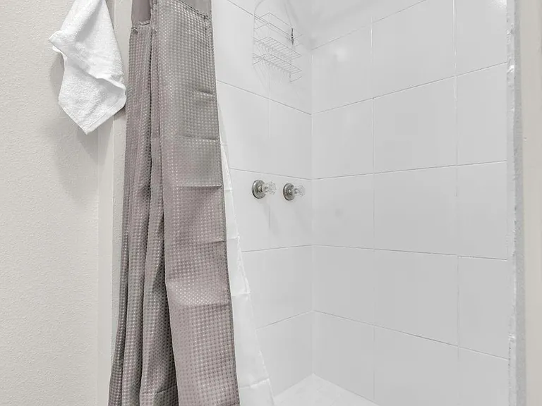 Tiled walk-in shower with curtain rod, handheld showerhead, and built-in wire caddy for convenient storage.