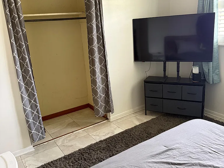 Bedroom with tile flooring, a dedicated closet with hanging storage, and space for a dresser and TV setup.