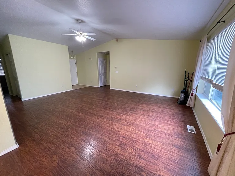 Living room view from dining area. Open door to main bedroom. Front door entry to the left of the open door. Ceiling fan.