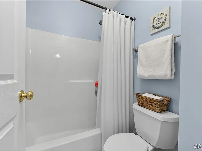 Bathroom featuring a white tub-shower combination, a standard toilet, and light blue wall paint