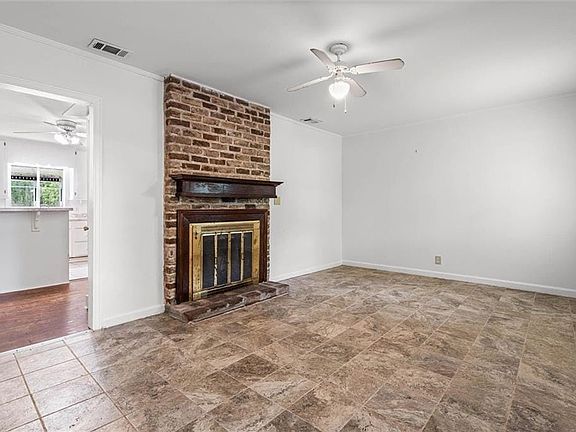 Unfurnished living room with a ceiling fan, ornamental molding, a fireplace, and stone finish flooring