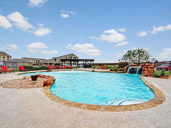 An outdoor pool for resident use surrounded by lounge chairs and a small waterfall