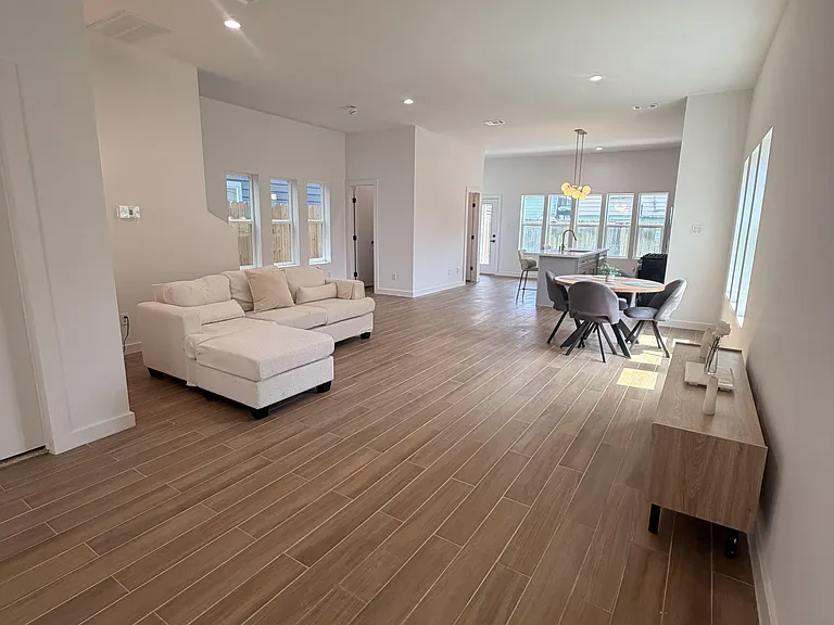 Open-concept living area with wood-look tile floors, recessed lighting, and large windows connecting to the kitchen/dining sp