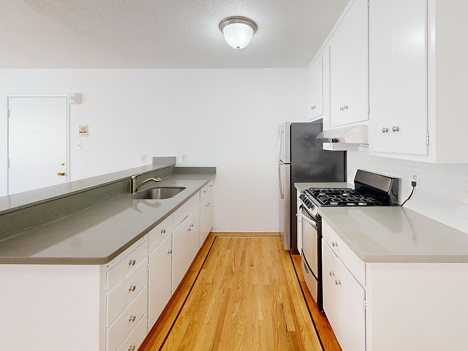Kitchen with multiple cabinets, refrigerator, stove, range hood, and sink