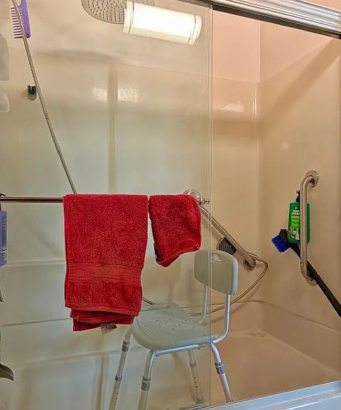 Shower has sliding glass doors and assist grab bars assist shower tub chair is stored in the adjacent closet storage area