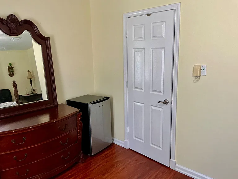 Bedroom corner with hardwood floors, a dresser with mirror, and a convenient mini-fridge for in-room snacks and drinks.
