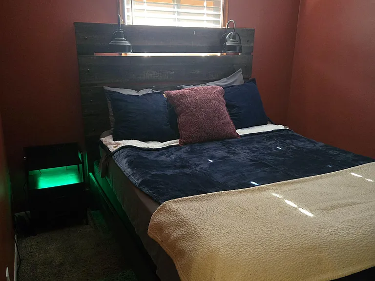 Furnished bedroom with full bed, rustic headboard, and window with blinds for light and privacy.