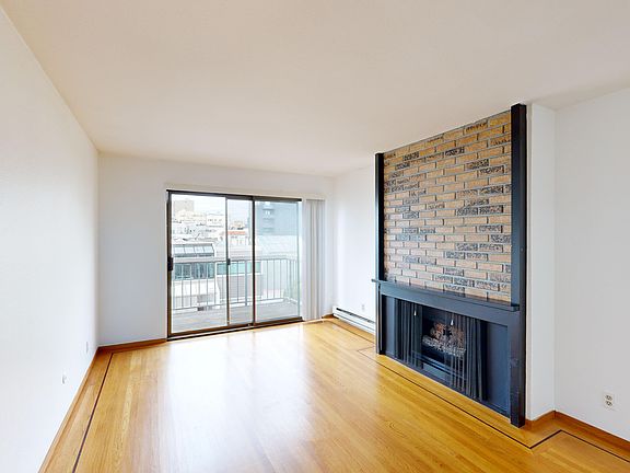 Spacious room with wood-like flooring, a large window offering natural light, and a fireplace