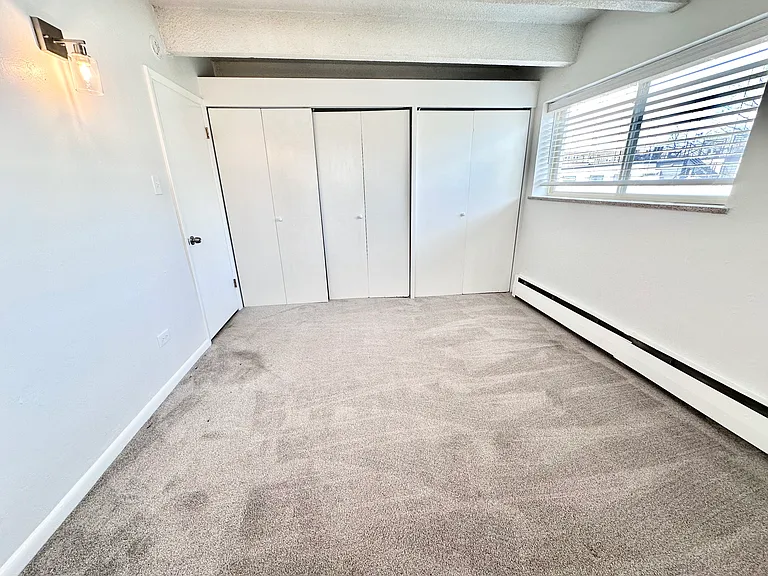 Bright, spacious bedroom with plush carpeting and large window featuring elegant blinds, enhancing natural light and offering a modern, cozy feel. Bright, spacious bedroom with plush carpeting and large window featuring elegant blinds, enhancing natural l