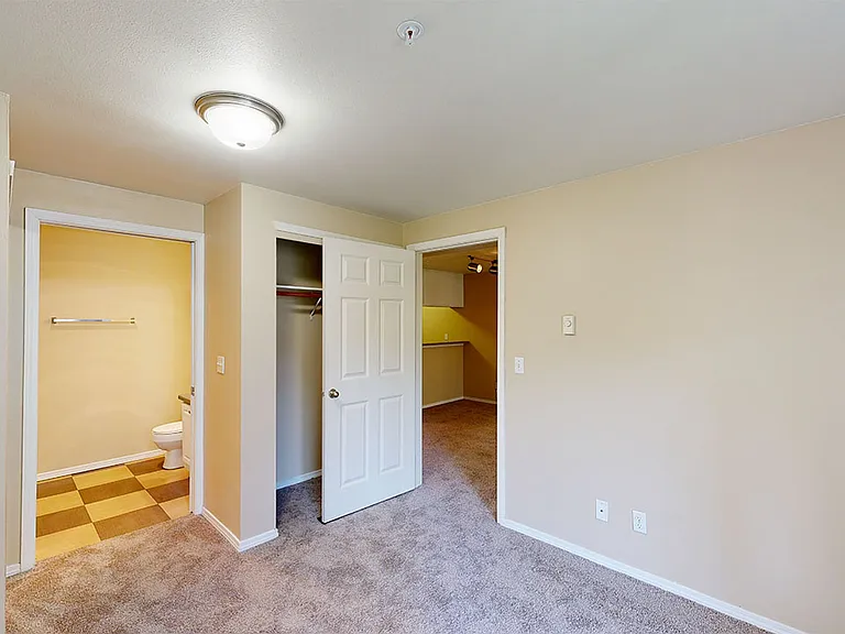 Spacious apartment bedroom with attached bathroom and plush carpet flooring.
