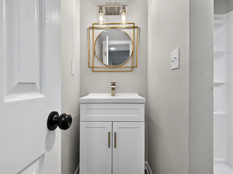 Updated bathroom vanity with sleek faucet, framed mirror, and overhead lighting, plus an easy-clean tub/shower surround.