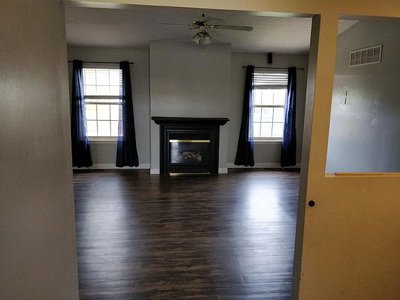 View from the front door / foyer of open living room with fireplace, ceiling fan, lots of light, and laminate flooring.