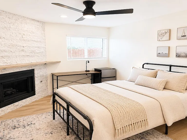 Spacious bedroom with a ceiling fan, large window, and a dedicated desk area plus mini fridge for added convenience.