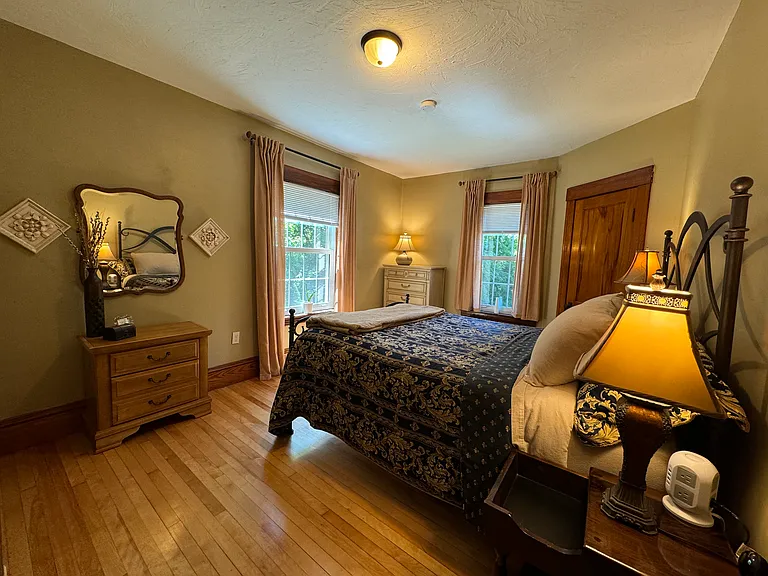 This corner back bedroom is right off the bathroom. It's accompanied with overhead lighting, 3 additional lamps, a queen size bed, a second wall mirror, curtains and blackout mini blinds and sumptuous bedding.