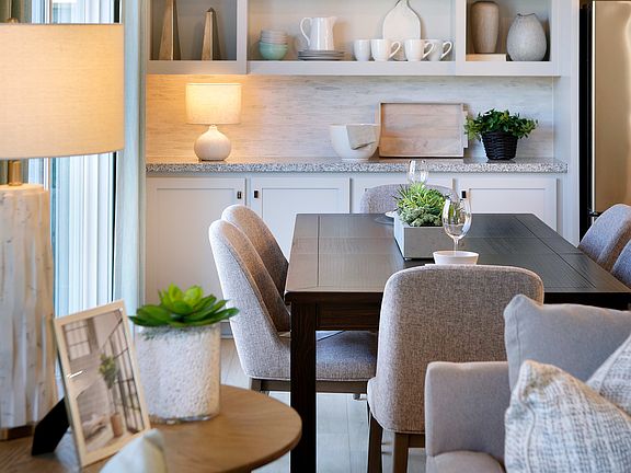 A cozy and inviting dining area with a wooden table, plush gray chairs, and open shelving displaying