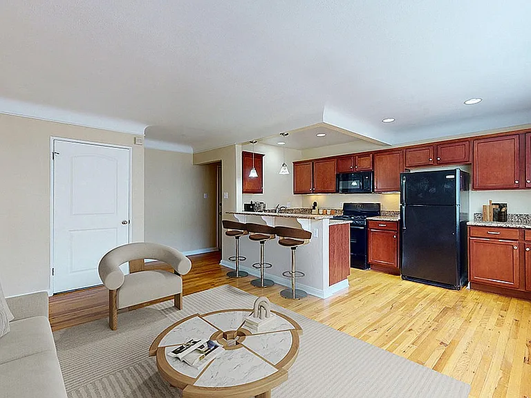 Inviting open-concept living area featuring a cozy sofa, stylish kitchen with elegant wooden cabinets, and a breakfast bar with modern stools.